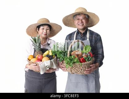 Zufriedenes südkoreanisches Seniorenehepaar, das Körbe mit frischem Obst und Gemüse vor weißem Hintergrund hält. Stockfoto