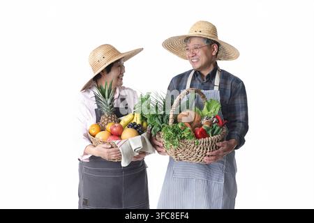 Zufriedenes südkoreanisches Seniorenehepaar, das Körbe mit frischem Obst und Gemüse vor weißem Hintergrund hält. Stockfoto
