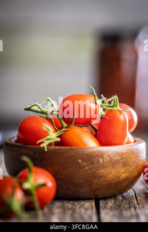 Hellrote Kirschtomaten, die in einer rustikalen Holzschale auf einem verwitterten Holztisch gestapelt sind, erinnern an Frische, Farm-to-Table-Kochen, gesunde Ernährung und vi Stockfoto