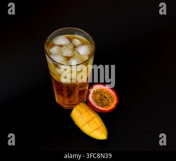 Fruchtsaft aus Mango und Passionsfrucht in einem hohen Glas mit Zitrone auf schwarzem Hintergrund, Stücke reifer Früchte in der Nähe. Nahaufnahme. Stockfoto