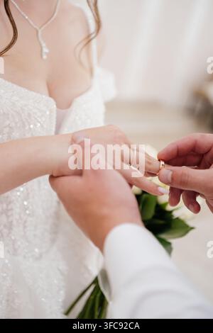 Nahaufnahme eines Bräutigams, der einem unerkennbaren Braut einen goldenen Ehering an den Finger steckt, die ein Paillettenkleid mit einem Anhänger-Halsband trägt. Stockfoto