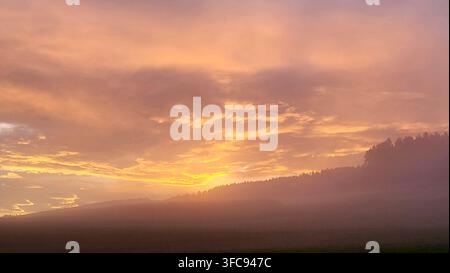 Malerischer nebliger Sonnenaufgang in sanften Orangetönen in der Schweiz Stockfoto