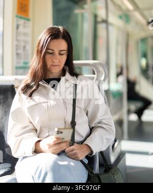 Mädchen, das in einem modernen Straßenbahnwagen sitzt, blättert durch Social Media Feed Stockfoto