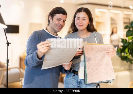 Porträt eines Mannes, der einer jungen Frau Polsterproben in einem Möbelgeschäft präsentiert Stockfoto