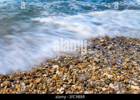 Wellen spülen über einen farbenfrohen Kieselstrand in North Landing, Flamborough Head an der Küste von Yorkshire, England. Stockfoto