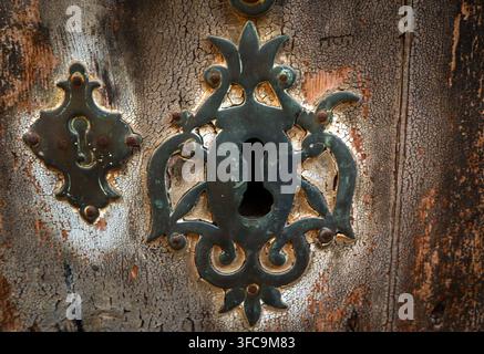 Nahaufnahme eines vintage Schlüssellochs mit einer verzierten Metallplatte, die auf einer rissigen Holztür montiert ist. Stockfoto