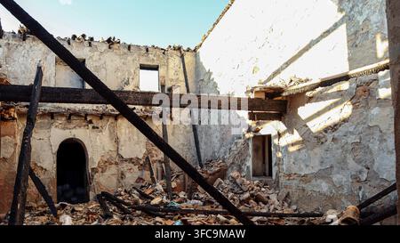 Innenansicht eines zerstörten Hauses nach einem Brand mit verkohlten Holzbalken, eingestürztem Dach und Trümmern. Stockfoto