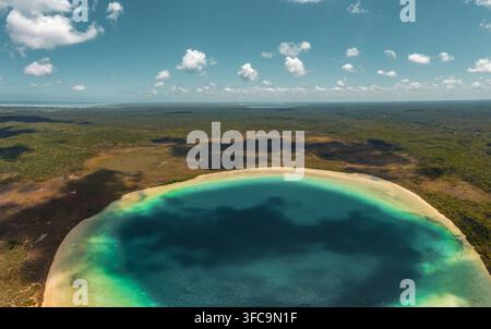 Luftaufnahme eines runden Cenotes mit türkisfarbenem Wasser, umgeben von üppigem Dschungel und Wald unter einem bewölkten Himmel in Tulum, Quintana Roo, Mexiko. Stockfoto