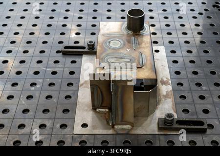Geschweißtes Stahlbauteil, das auf einem modularen 3D-Schweißtisch mit Rasterbohrungen in einer industriellen Metallwerkstatt eingespannt ist Stockfoto