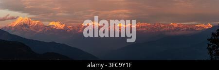 Ein weitläufiges Panorama der Himalaya-Himmelssilhouette, die bei Sonnenuntergang orange und rosa leuchtet, mit dunklen Vorberg-Silhouetten, die sich unter den beleuchteten Gipfeln schichten. Stockfoto