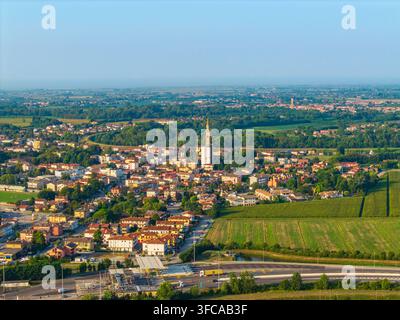 Luftbild der Stadt Noventa di Piave mit ihrem zentralen Kirchturm, Wohndächern, grünen Feldern und einer Autobahn in Noventa di Piave Stockfoto
