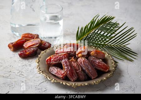 Glas Wasser und trockene Datteln auf einem traditionellen Teller über Marmorhintergrund für das Ramadan-Iftar-Konzept Stockfoto