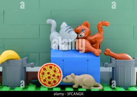 Tambow, Russische Föderation - 03. August 2026 Zwei Lego-Katzen und eine Maus-Minifigur suchen nach Nahrung wie Pizza und Hühnchen in der Nähe von Mülltonnen. Stockfoto