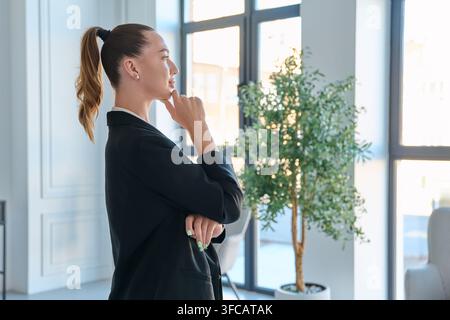 Nachdenkliche Geschäftsfrau schaut aus dem Fenster im Büro Stockfoto