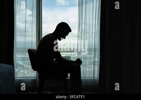 Trauriger Mann in einem dunklen Raum voller Verzweiflungsgedanken. Porträt eines nachdenklichen traurigen Mannes allein. Angst, Traurigkeit, Missbrauch, Depression, Sucht. Stockfoto