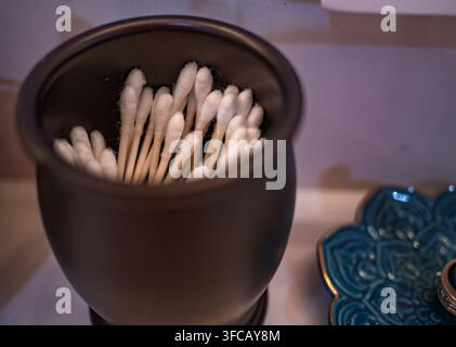 Baumwollstäbchen, die in einem dunkelbraunen Keramikbehälter auf einer Waschtischoberfläche aufbewahrt sind Stockfoto