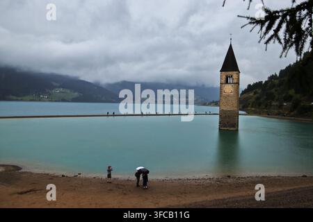 CURON, ITALIEN, 20. AUGUST 2026: Der berühmte, teilweise versunkene Glockenturm aus dem 14. Jahrhundert der alten Kirche von Curon, der aus dem türkisfarbenen Wasser aufsteigt Stockfoto