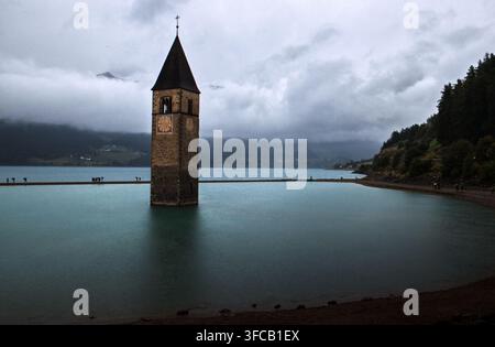 Eine Panoramaaufnahme des berühmten untergegangenen Glockenturms von Curon Venosta, der aus den türkisfarbenen Gewässern des Reschensees in Südtirol auftaucht. Stockfoto