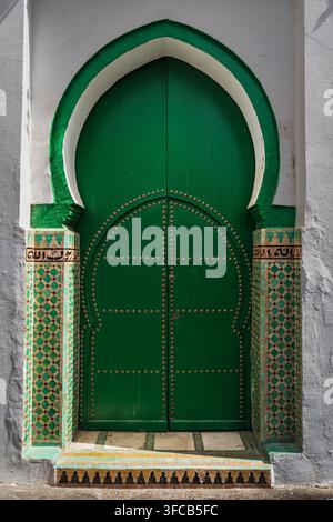 Traditionelle grüne Holztür mit gebogenem Rahmen und dekorativen Metall-Zellij-Mustern in der alten Medina von Asilah, Marokko. Stockfoto