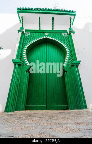 Grüne hölzerne Eingangstür, eingerahmt von einem gebogenen Rahmen mit authentischen marokkanischen architektonischen Details in der Medina von Asilah, Marokko. Stockfoto