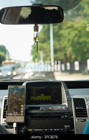 Ansicht aus dem Inneren eines fahrenden Taxis, wobei das Armaturenbrett eine Navigationskarten-App auf einem Smartphone und den Energiebildschirm anzeigt. Stockfoto