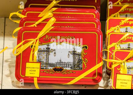 Rote Dosen, die mit gelben Bändern versehen und mit "Bergamotes Adam Nancy" beschriftet sind, stehen in einem Schaufenster in Nancy, Grand Est, Frankreich. Die Kunst auf der Dose zeigt die vergoldeten Grilles de Jean Lamour auf dem Place Stanislas. Stockfoto