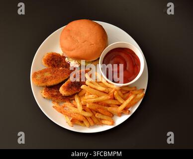 Ein Burger, Pommes und gebratene Hühner Nuggets mit Ketchup auf einem runden Teller vor schwarzem Hintergrund. Top-Down-Ansicht, Flat Lay. Stockfoto