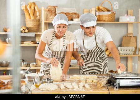 Bäckermädchen und Bäckerjunge arbeiten als Bäcker in der Bäckerei, kneten und schneiden den Teig in Stücke und wiegen jedes Stück. Während der Arbeit mit dem Teig wiegt der Arbeiter den Teig und s Stockfoto
