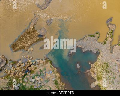Luftaufnahme der Mündung von trübem braunem Flusswasser und klarem blaugrünem Wasser mit felsigen Ufern und Kiesbänken in Indonesien. Stockfoto