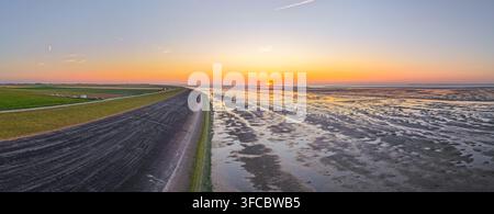 Luftaufnahme des Sonnenuntergangs über den Wattenmeer-Schlammflächen nahe des Eemshaven-Damms, mit goldenem Licht, das sich auf den nassen Gezeitenflächen spiegelt, und einem klaren Horizont Stockfoto