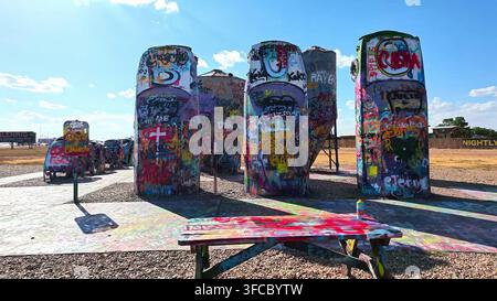 AMARILLO, TX, USA - 20. MAI 2026: Ein hölzerner Picknicktisch steht vor den mit Graffiti bedeckten vergrabenen Autos am Cadillac Ranch Outdoor-Kunstort in Am Stockfoto