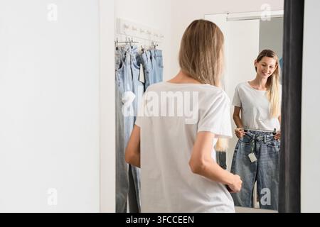 Einzelhandels-Einkauferlebnis, junge Frau, die Jeans in einer Umkleidekabine anprobiert, Mode und Konsumverhalten Stockfoto