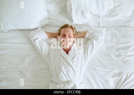 Lächelnder Mann im Bademantel entspannt sich auf dem Bett in einem Luxushotelzimmer Stockfoto