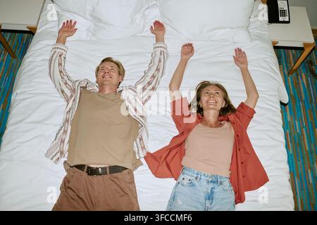 Glückliches Paar liegt im Hotelzimmer auf dem Bett und feiert die Ankunft des Urlaubs Stockfoto