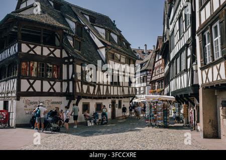 Touristen erkunden eine Kopfsteinpflasterstraße, die von traditionellen Fachwerkhäusern gesäumt ist, im historischen Zentrum von Straßburg, Elsass, Frankreich. Stockfoto