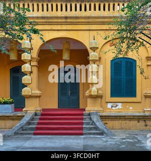 Traditionelles gelbes Gebäude im kolonialen Stil in der Kaiserfestung Thang Long in Hanoi, Vietnam, mit einem gewölbten Eingang und einem roten Teppich Stockfoto