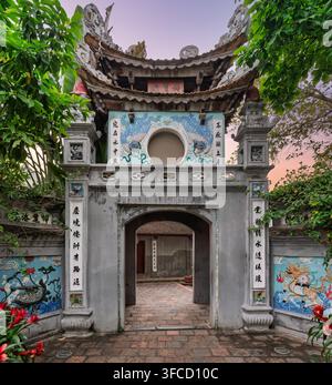 Aufwendig geschnitztes traditionelles Steintor am historischen Bach-Ma-Tempel in Hanoi, Vietnam, mit detaillierter chinesischer Kalligraphie und farbf Stockfoto