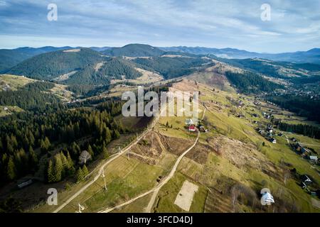 Luftaufnahme einer atemberaubenden Berglandschaft mit sanften Hügeln, dichten Wäldern und ländlichen Häusern. Kurvenreiche Schotterstraßen führen durch Felder und verbinden die kleinen Häuser und Farmen. Stockfoto