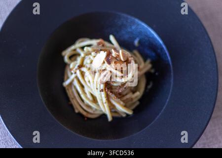 Hochwinklige Soft-Focus-Ansicht von Vollkornspaghetti mit cremiger Sauce, Mandelblättern und Paniermehl in einer dunklen Keramikschüssel Stockfoto