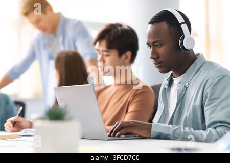 Gruppe verschiedener Menschen, die am Tisch sitzen, arbeiten, für einen Test lernen, gemeinsam an einem Projekt oder Hausaufgaben arbeiten, selektiver Fokus auf afroamerikanischen Mann Stockfoto