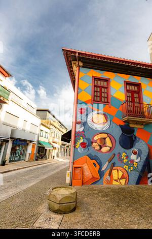 Amarante, Douro-Tal, Portugal Lebendiges Wandgemälde schmückt ein farbenfrohes Gebäude in der historischen Stadt. Straßenszene zeigt Kopfsteinpflaster und ruhige Ladenfronten. Blau Stockfoto