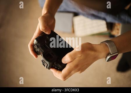 Hände einer jungen kaukasischen Frau, die eine professionelle spiegellose Kamera hält und die Einstellungen vornimmt. Bild repräsentiert Fotografieausbildung, kreatives Hobby oder digitale Inhaltsgestaltung, Blick aus hohem Winkel Stockfoto