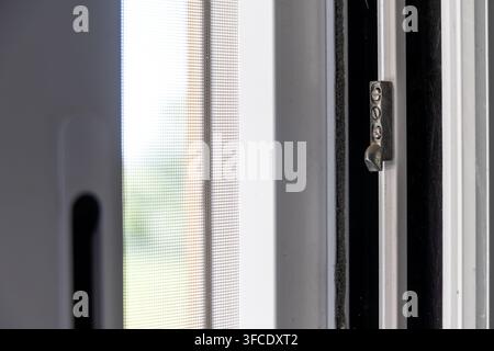 Detaillierte Ansicht eines feinen Maschenfenstersiebs und eines Metallriegels an einem weißen Fensterrahmen, der Textur und Konstruktion zeigt Stockfoto