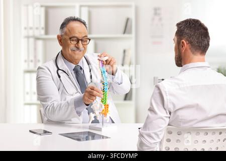 Arzt zeigt einem männlichen Patienten ein Wirbelsäulen-Bone-Modell im Büro Stockfoto