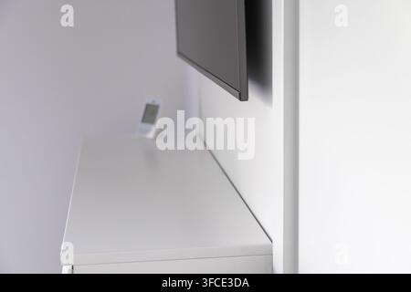 Ein schlanker, zeitgenössischer Wohnraum mit einem Flachbildfernseher, der über einer weißen Kommode montiert ist, auf der ein kleines elektronisches Gerät steht Stockfoto