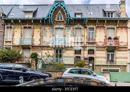 Ein Jugendstilhaus mit bemalten floralen Fassadenmotiven und türkisfarbenen Holzbalustern steht in der Rue Félix Faure in Nancy, Grand Est, Frankreich, mit zwei davor geparkten Autos. Stockfoto