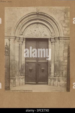 Dom in Mainz, Fotografie, Fotograf: Carl Hertel, Mainz, 1850 - 1900, Rheinland-Pfalz, Papier, Albumen-Druck, Höhe 250 mm x Breite 190 mm, Höhe 320 mm x Breite 210 mm, Mainzer Dom. Ein großes, verziertes Steintor mit doppelten Holztüren, eingebettet in ein geschnitztes gewölbtes Portal; das Gewölbe enthält skulpturale Reliefs, darunter eine zentrale sitzende Figur, flankiert von zwei weiteren Figuren und umgeben von dekorativen Mustern, und das Gewölbe ist von geschichteten halbrunden Profileinfassungen umrahmt. Säulen mit geschnitzten Kapitellen flankieren das Tor, und die Steinmauern auf beiden Seiten zeigen texturierte, verwitterte Mauerarbeit. Der Stockfoto