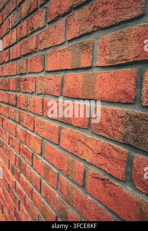 Vollformat rote Ziegelwand mit abwechslungsreichen handgefertigten Ziegeltexturen und dunklen Mörtelverbindungen, die einen warmen architektonischen Hintergrund bilden Stockfoto