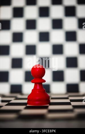 Einziger roter Schachbauer auf einem schwarz-weißen Schachbrett mit unscharfem Schachbrett-Hintergrund und großzügigem Kopierraum oben Stockfoto