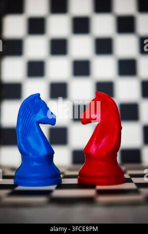 Blaue und rote Schachspringer stehen sich auf einem schwarz-weißen Schachbrett gegenüber und deuten auf Rivalität, Strategie und Konfrontation hin Stockfoto